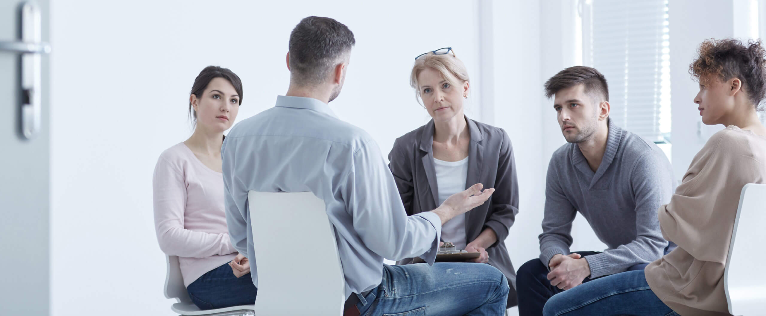 A group of five people sit in a circle as part of a group counselling session.