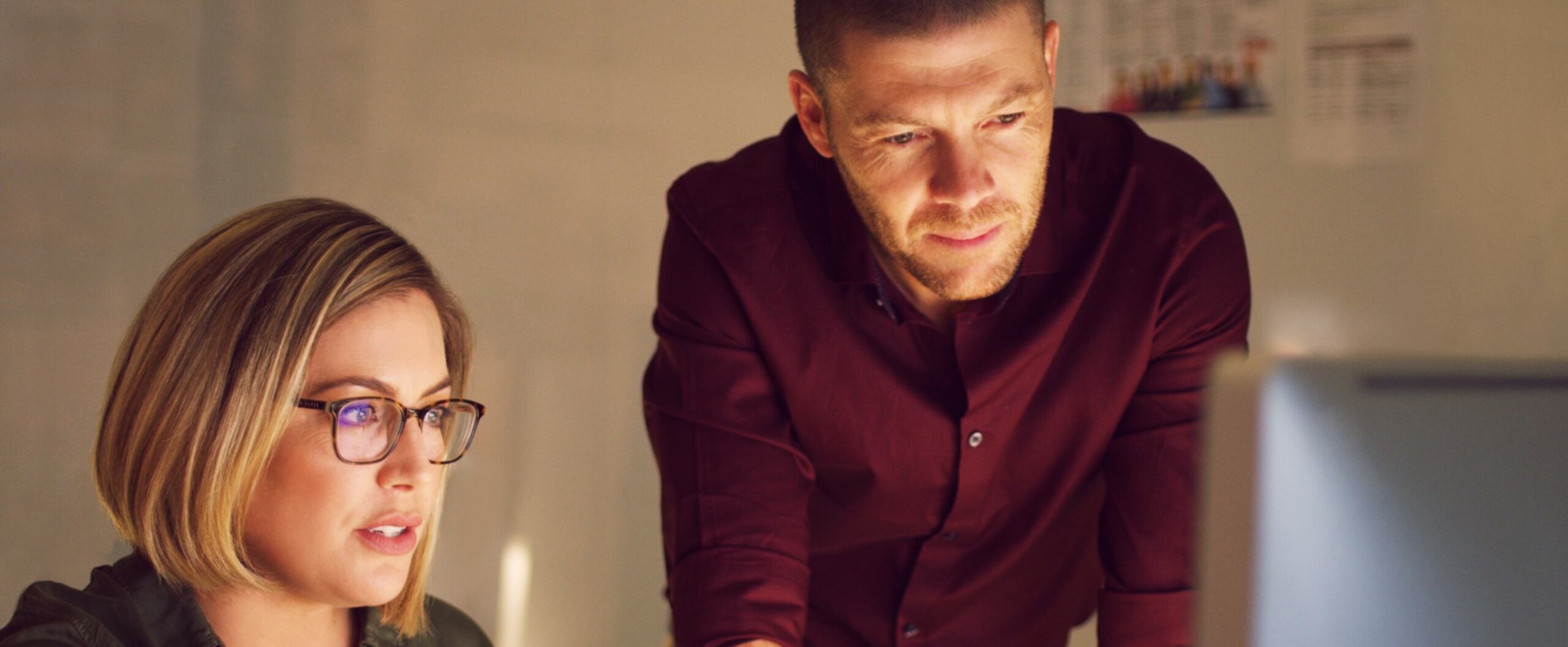 A woman with glasses sitting at, and man standing over a desk looking at a desktop monitor | Bachelor of Psychological Science and Criminology