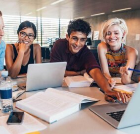 A group of students happily discuss something over laptops.