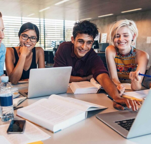 A group of students happily discuss something over laptops.