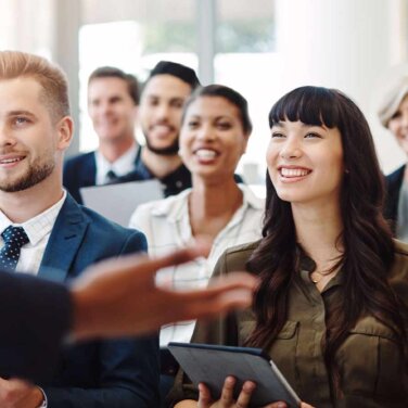 Diverse group of people sitting in a lecture, smiling.