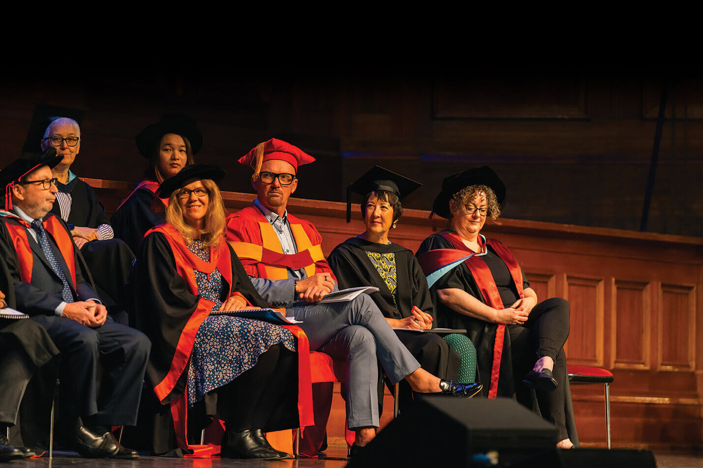 Academic staff sit on stage in traditional and ceremonial robes and caps
