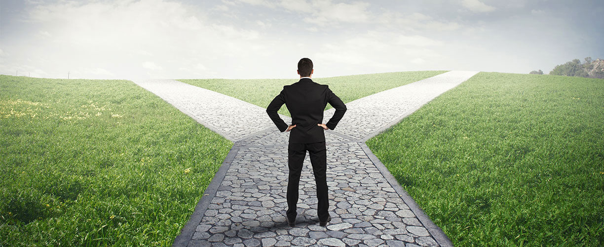 A businessman with hands resting on hips facing a crossroads