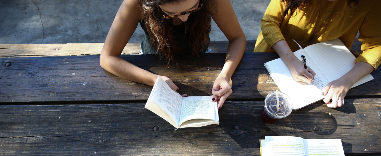 Students outside on a picnic table, reading and writing in books