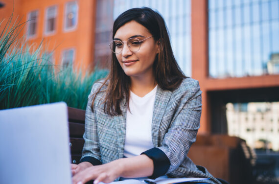 A female MBA student working on a laptop outside an office building