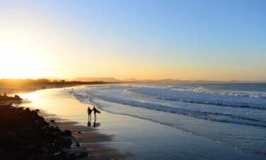 Two people walking along a beach in Byron Bay at sunrise