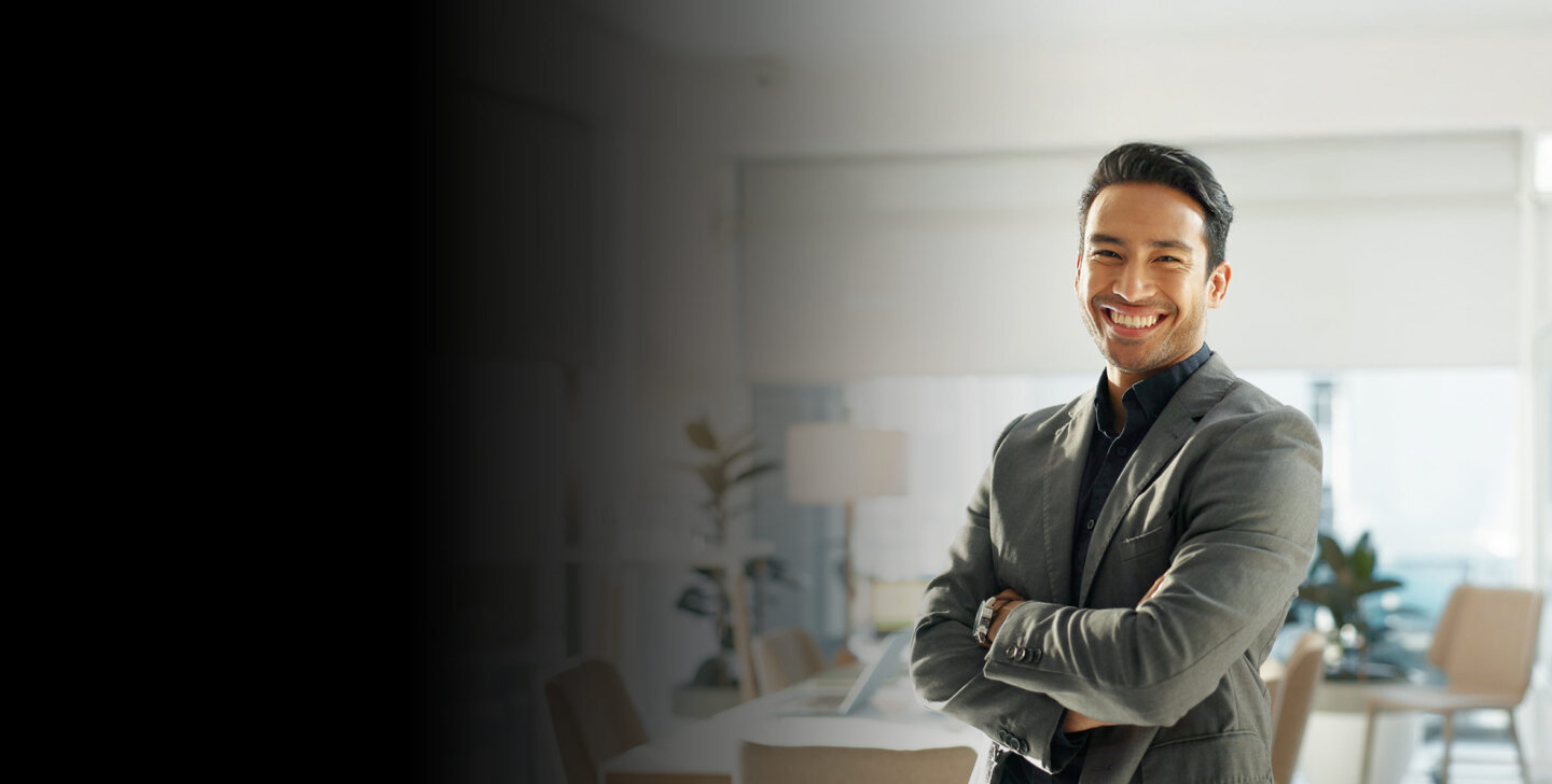 A man in a green and black shirt standing in an office with his arms folded, smiling towards camera - ACAP Master of Professional Accounting (2880x1188)