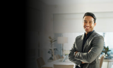 A man in a green and black shirt standing in an office with his arms folded, smiling towards camera - ACAP Master of Professional Accounting (2880x1188)