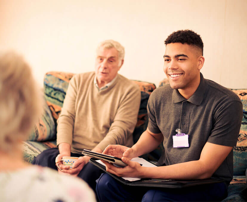 Young social worker sitting on the couch with an older man, with tablet in hand
