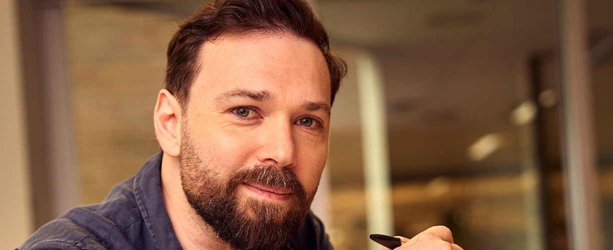 Alex holding a pen looking at the camera