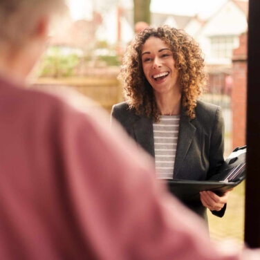 Smiling female social worker standing at the doorway of a client with a folder in hand