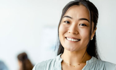 Woman smiles and looks to camera. Two figures are blurry in background.
