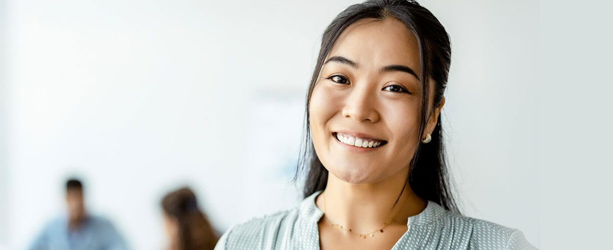 Woman smiles and looks to camera. Two figures are blurry in background.