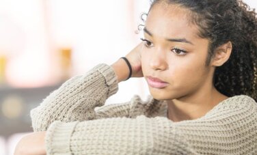 A woman looks down and has her hands on knees. One hand resting behind her ear.