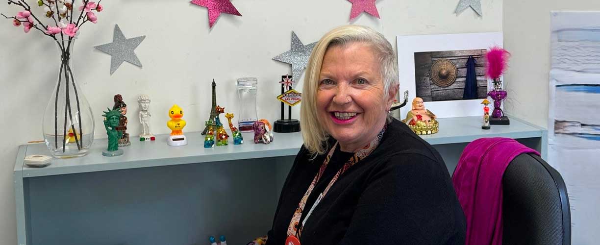 Woman sits in chair in front of desk with trinkets. Stars on wall. Flowers in vase.
