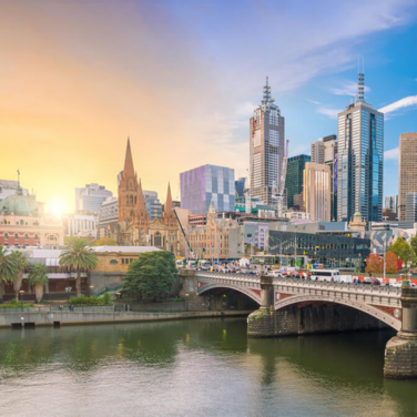 An image of cityscape and skyline. A river and bridge in foreground. City building and skyscrapers in background. Sun sets in background. Melbourne, Australia.