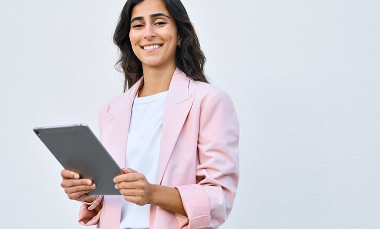 Woman stands in a pink jacket. With device.