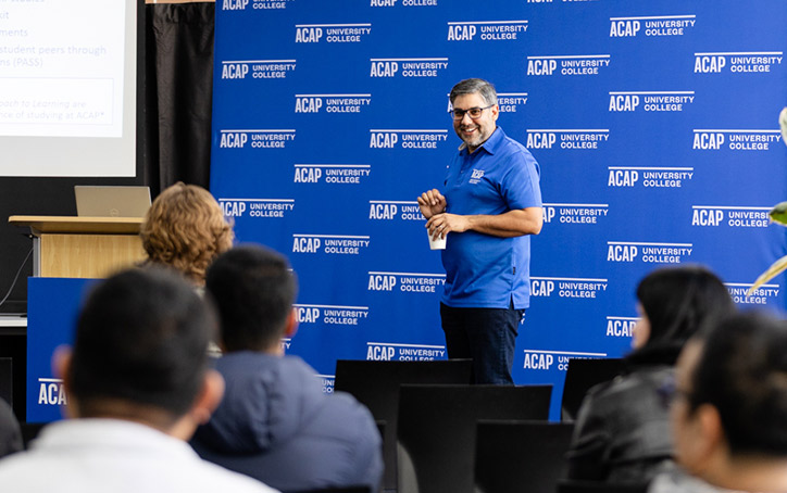 A male ACAP University college staff member standing in front of a seated crowd at and Info Night event (724x454)