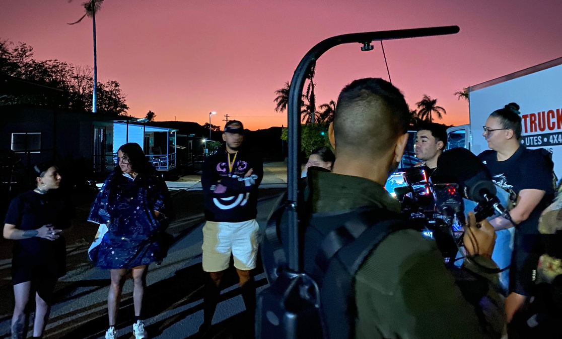 image of cameraman shot from behind in a sunset-lit scene flled with young people chatting in a parking lot