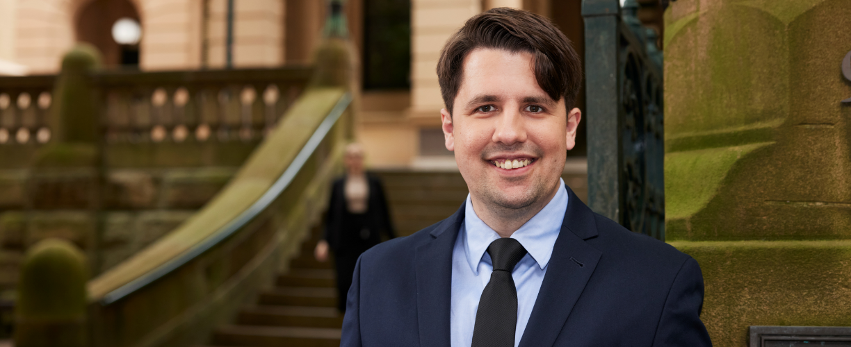 man in suit stands in front of sandstone building