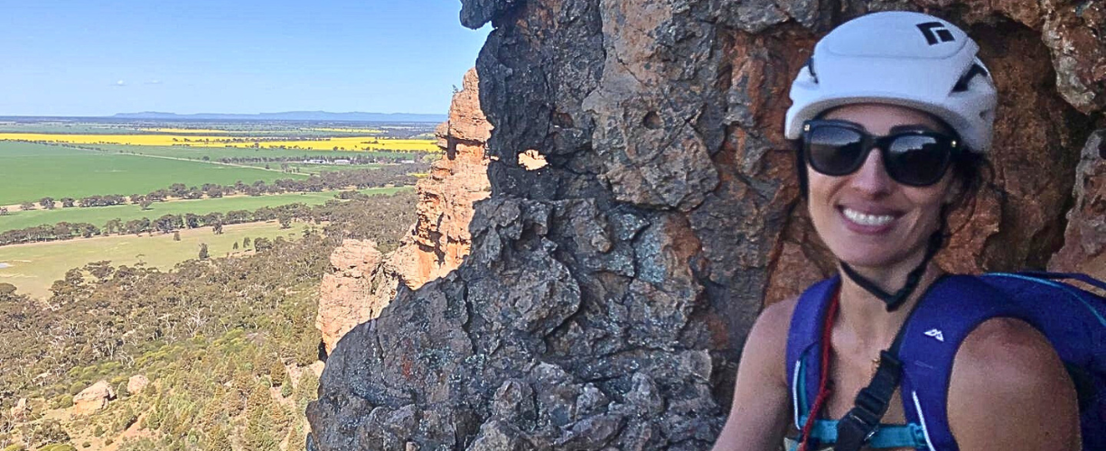 woman in climbing gear in front of rock with landscape in background