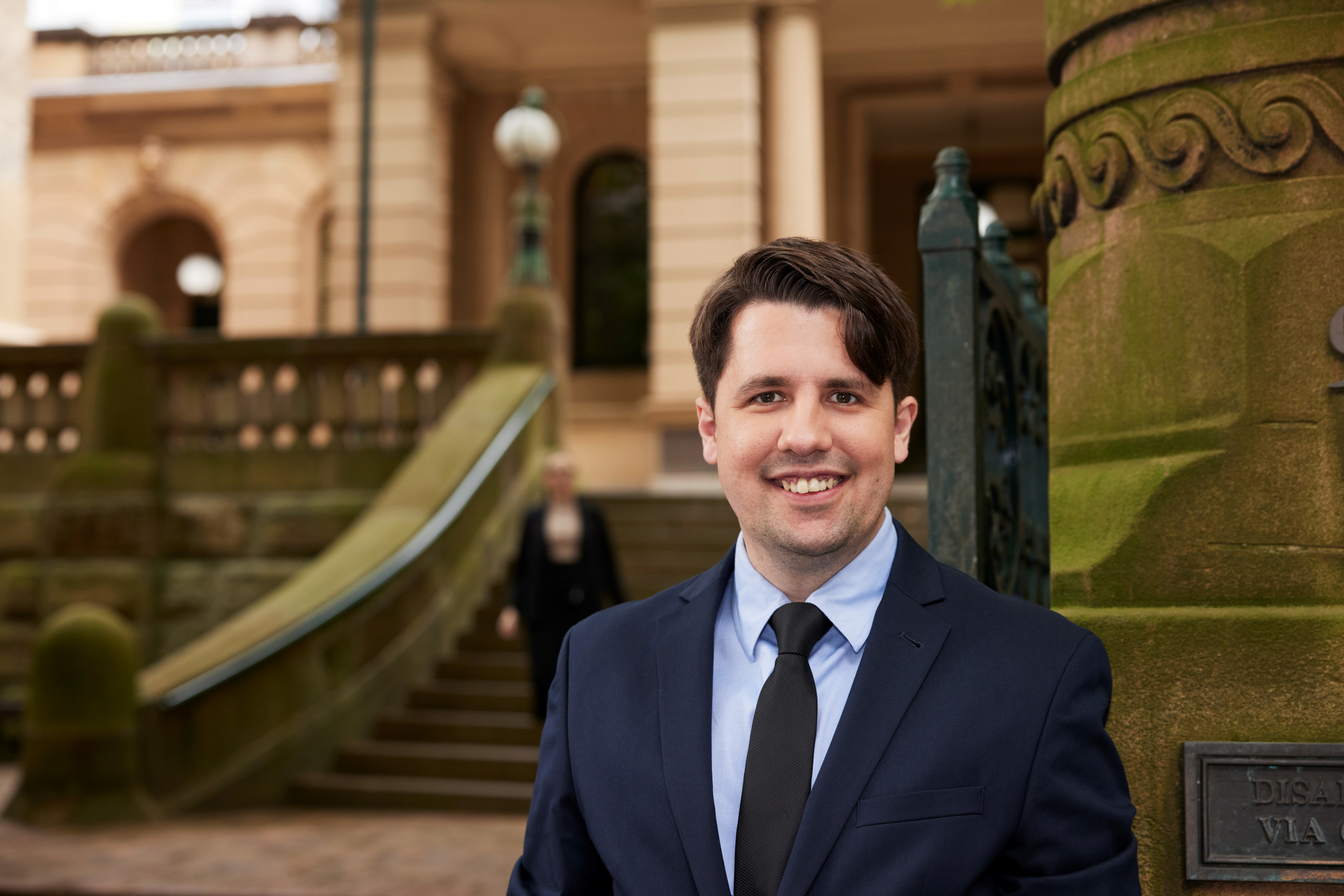 man in suit stands in front of sandstone building
