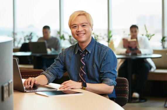 ACAP student Tidus sitting at a work space with a laptop, smiling towards camera