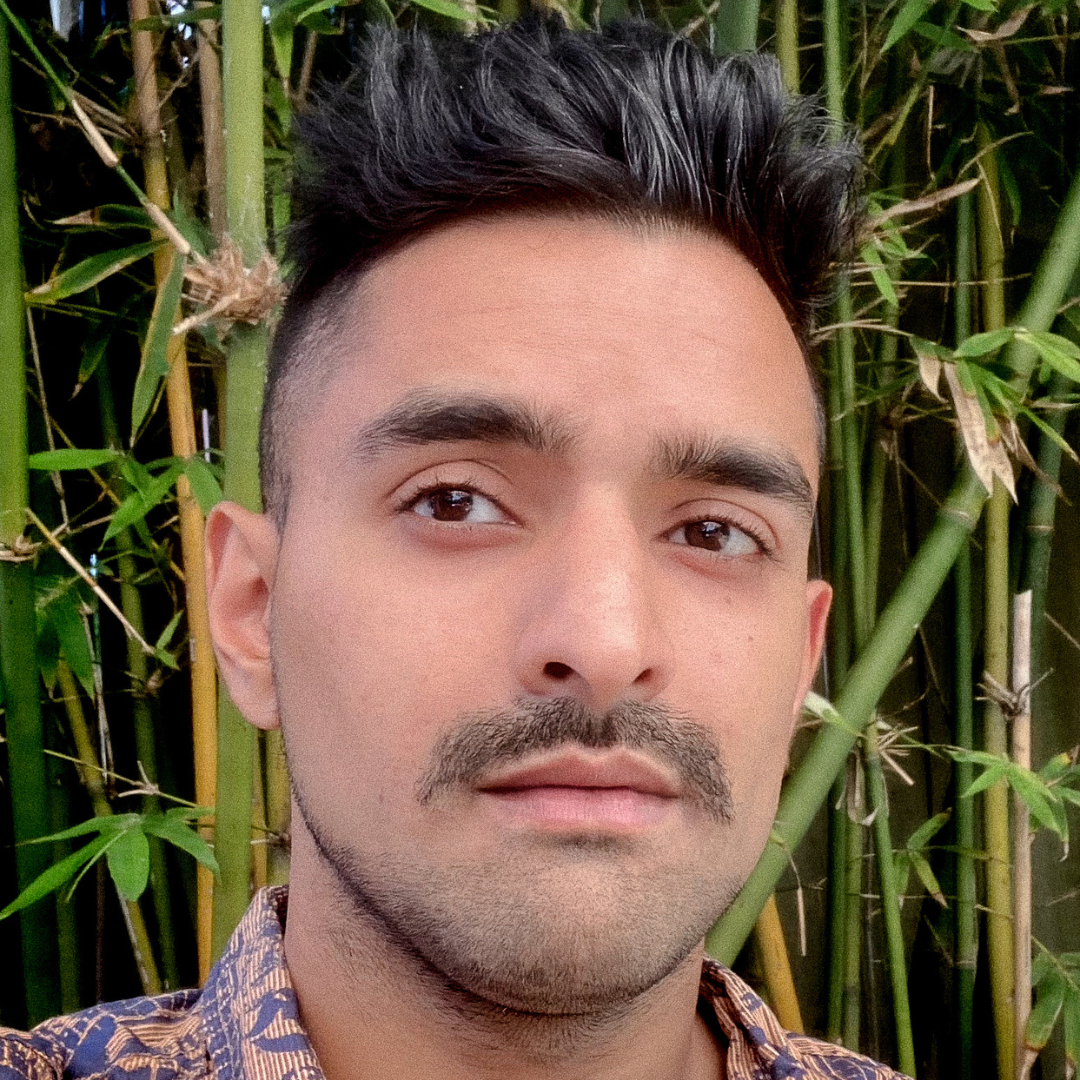 young man with dark skin and black hair in front of bamboo