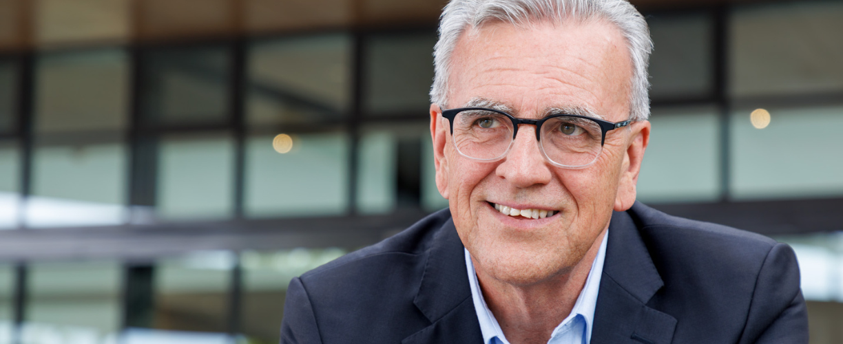 man with glasses and white hair looks into distance smiling in close up image