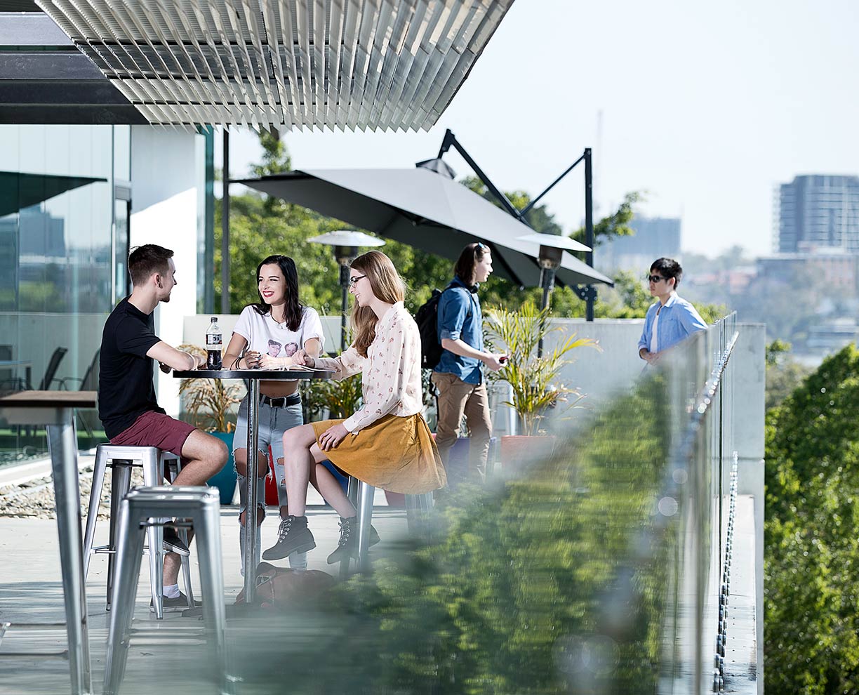 Three students sitting on an outdoor balcony area at a cafe in Brisbane