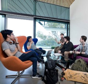 A group of five male students sitting on chairs around a glass table in front of a large window at ACAP Brisbane campus
