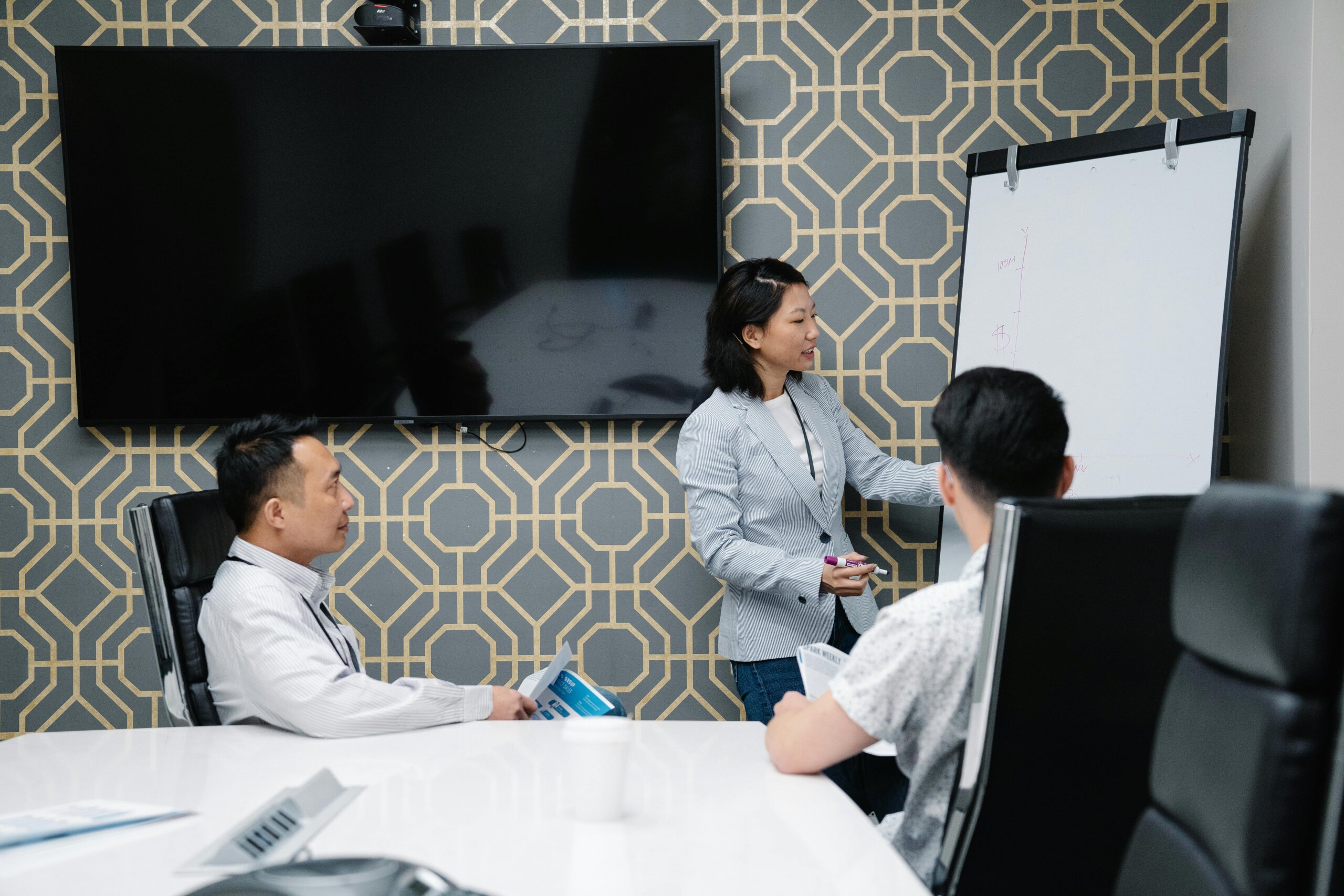 Woman presenting information on a whiteboard to two males.