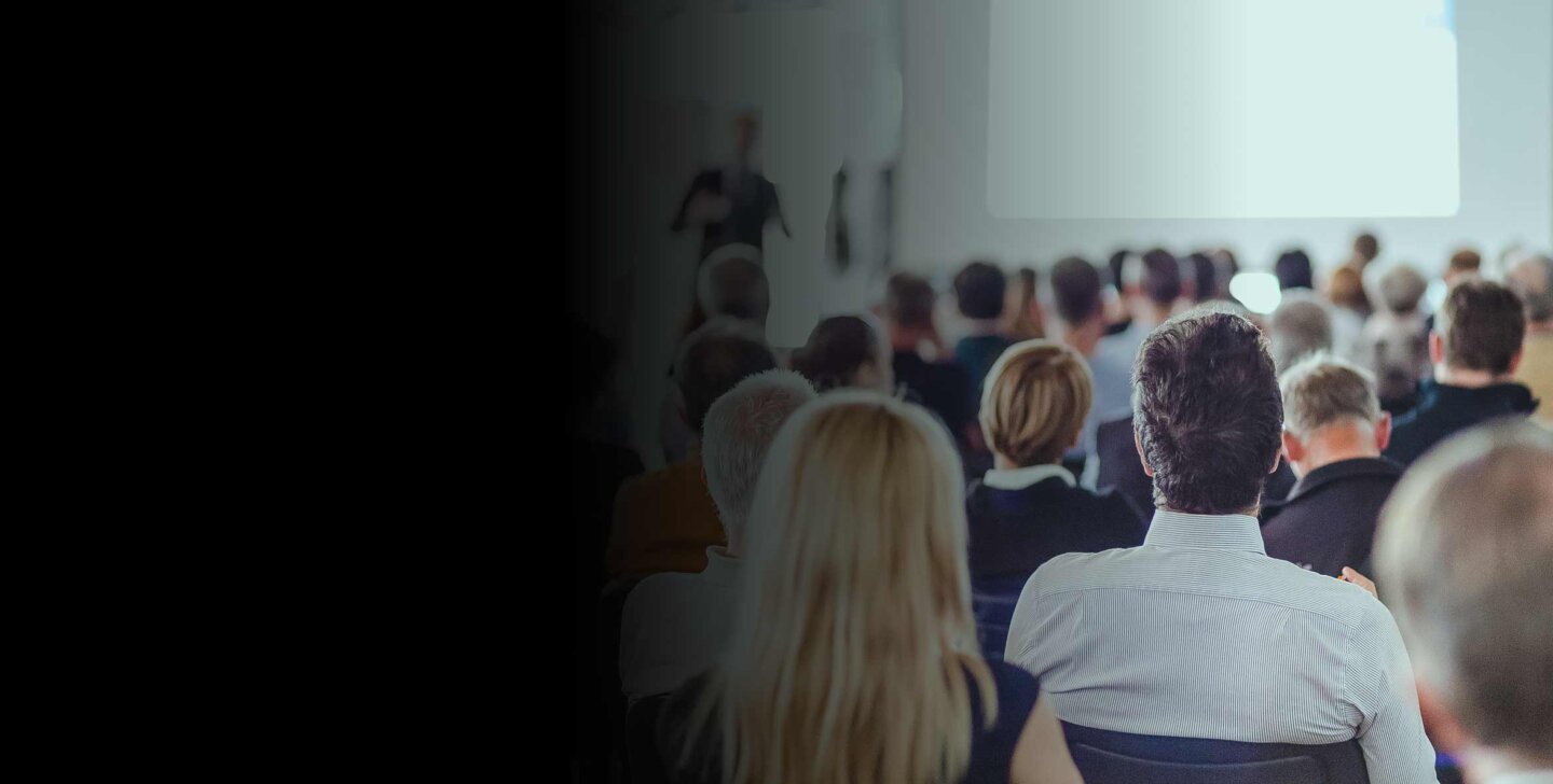 A group of academics sitting in chairs at a conference, facing with their backs to camera - ACAP Conference 2880x1188