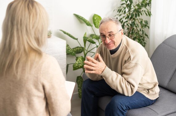 An adult man sitting in a counselling session with a female counsellor or psychologist (1140x752)