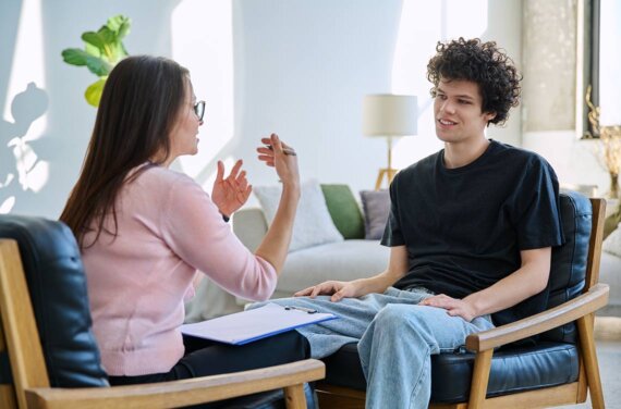 A young man sitting in a counselling session with a female counsellor or psychologist (1140x752)